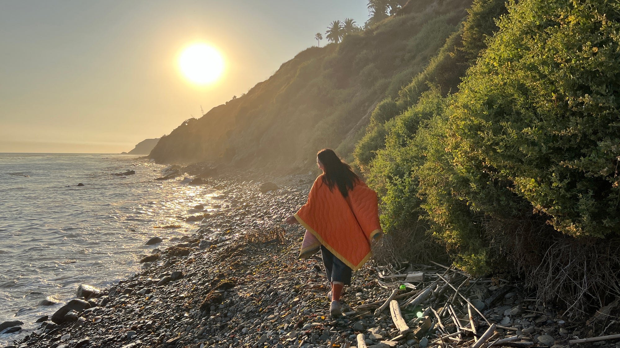 Women wearing a Scout Regalia Anywear Blanket or Poncho by the sea with the sun setting.