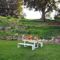 A white S.R. All Aluminum Table Set on grass with stone wall in background.
