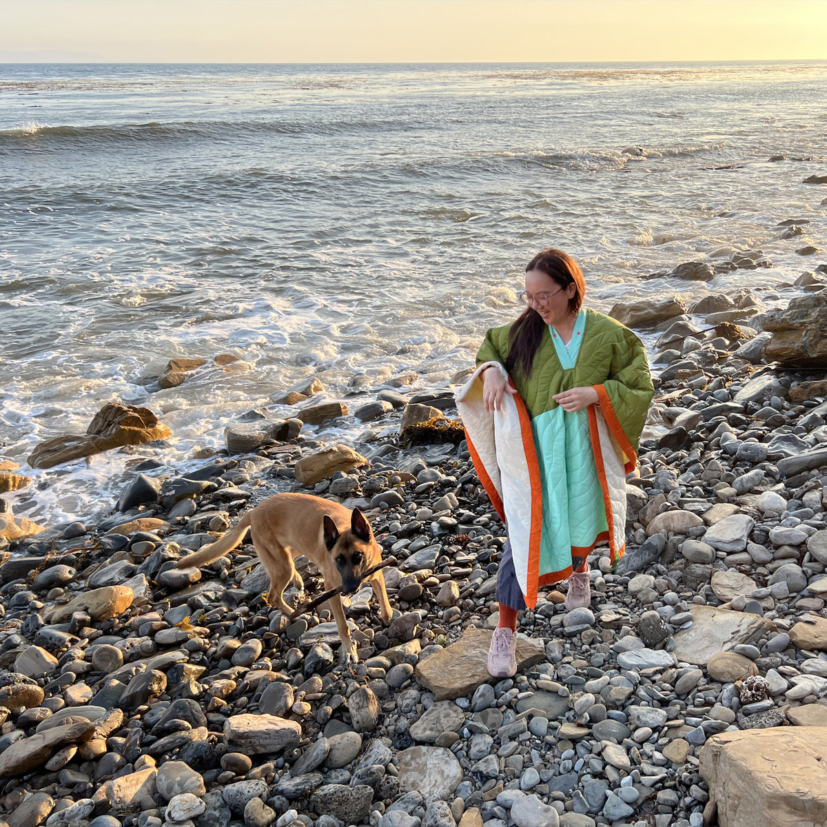 S.R. Anywear Blanket in Ocean Kelp. Woman wearing green and mint poncho on beach next to a brown dog