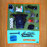 S.R. Anywear Blanket in Ocean Kelp. A collection of camping gear laid out on a green and mint blanket