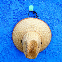 S.R. Anywhere Hook in Mint Green on a textured blue stucco wall, holding a large straw sun hat.