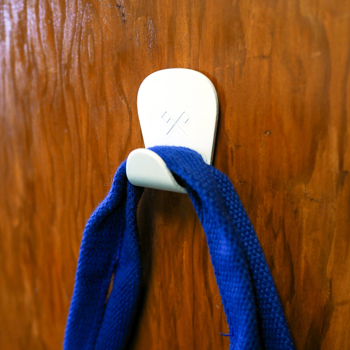 S.R. Anywhere Hook in Matte White on a wood wall holding a blue handle