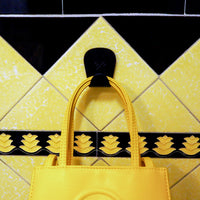 S.R. Anywhere Hook in Matte Black on a black and yellow tile wall, holding a yellow handbag