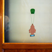Fern Green S.R. Anywhere Hook holding a tree shaped air freshener on a frosted glass door with a wood frame.