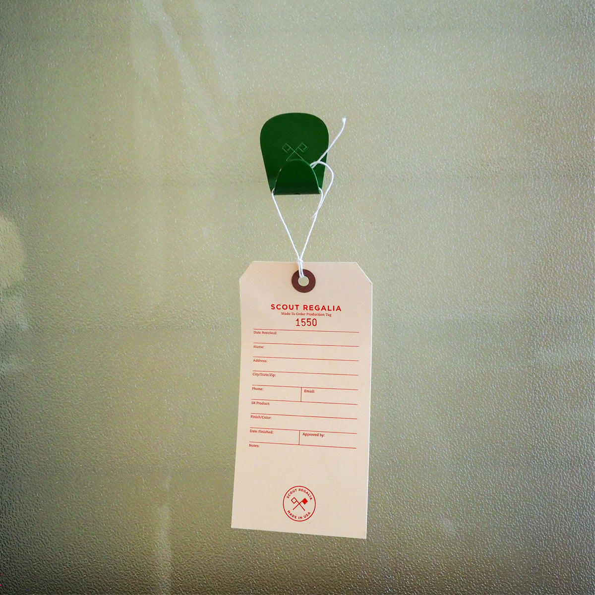 Fern Green S.R. Anywhere Hook holding a Scout Regalia hang tag on  frosted glass