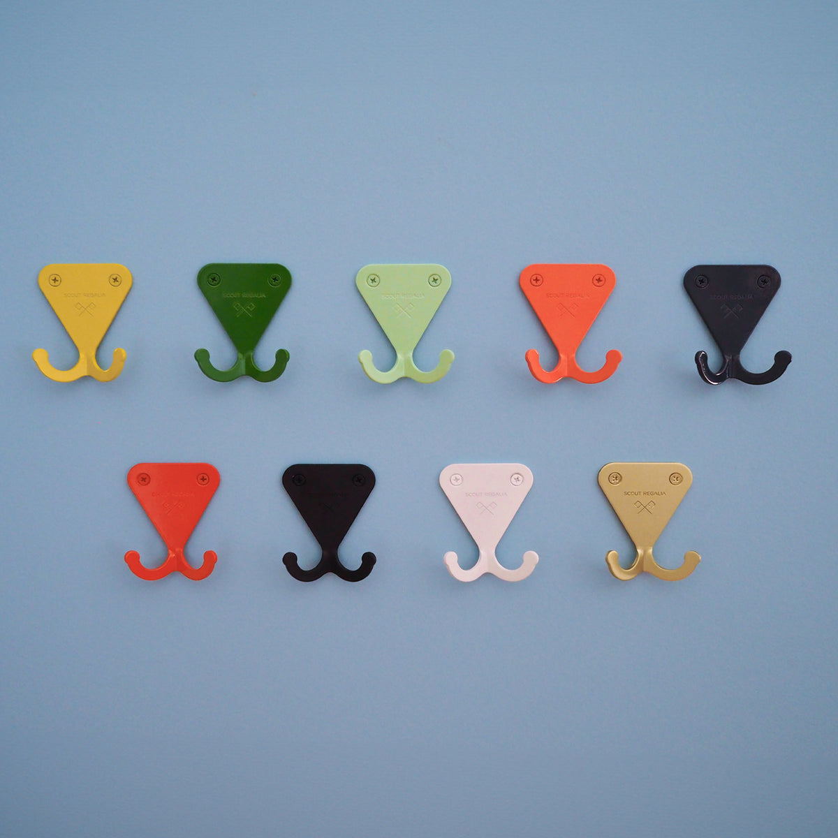 S.R. Wall Hooks on light blue background. From top left: Citrus Yellow, Fern Green, Mint Green, Salmon Pink, Navy Grey, Bright Orange, Matte Black, Matte White, and Anodized Brass.