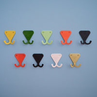 S.R. Wall Hooks on light blue background. From top left: Citrus Yellow, Fern Green, Mint Green, Salmon Pink, Navy Grey, Bright Orange, Matte Black, Matte White, and Anodized Brass.