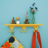 Citrus Yellow S.R. Wall Rack holding small vases of flowers and salt shakers on the shelf, with a potholder and red apron tie on the hooks.