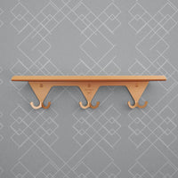 Anodized brass S.R. Wall Rack on a grey background with geometric print.
