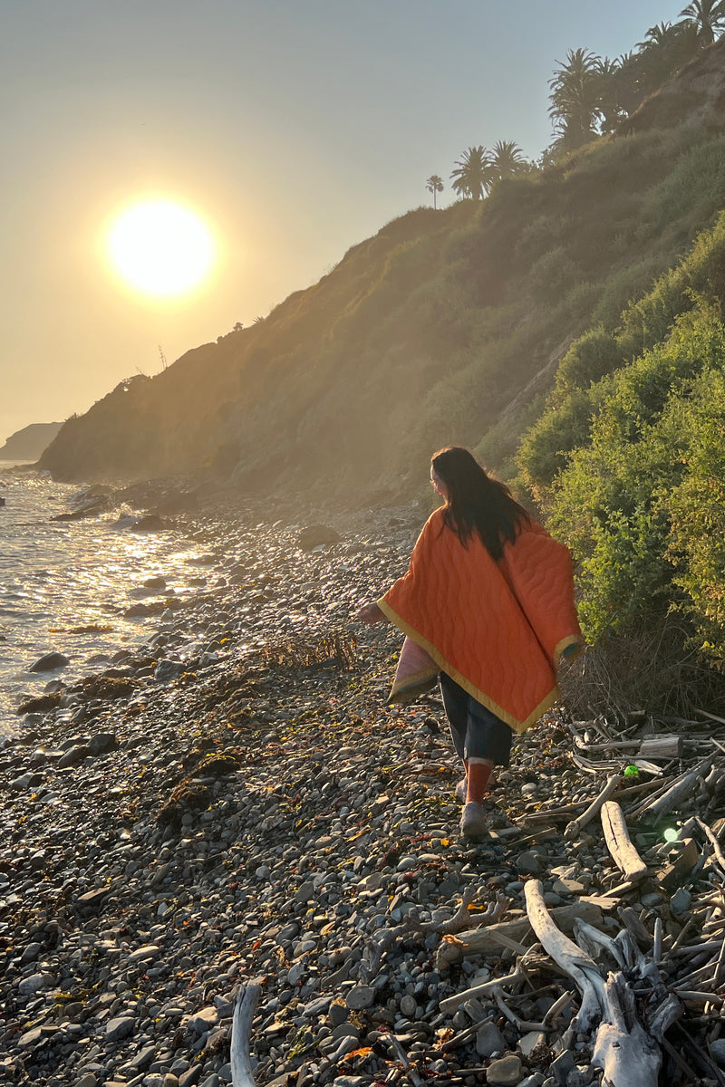 Women wearing a Scout Regalia Anywear Blanket or Poncho by the sea with the sun setting. 