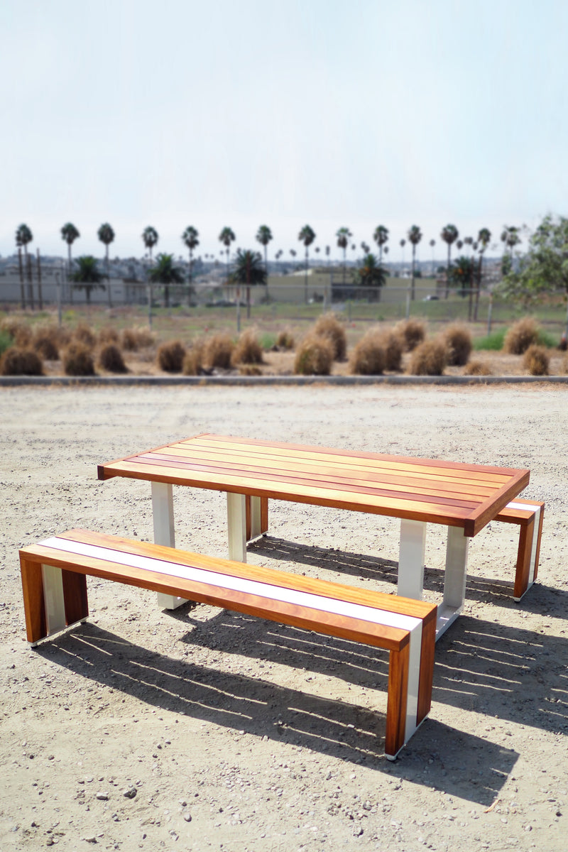 Scout Regalia Tabe Set with cream powder coated aluminum frame and  Iroko wood set on a gravel landscape.