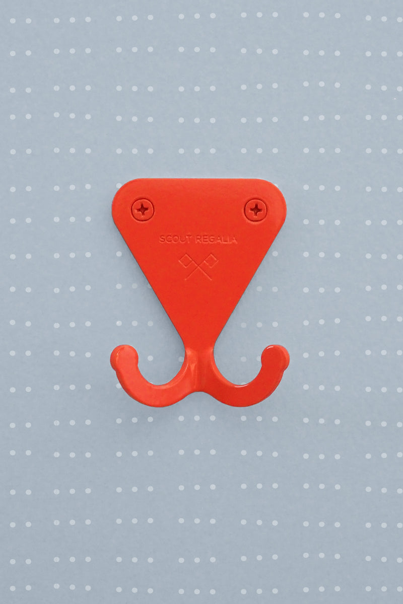 Scout Regalia Wall Hook in bright orange mounted on a light blue wallpaper with wavy dots.