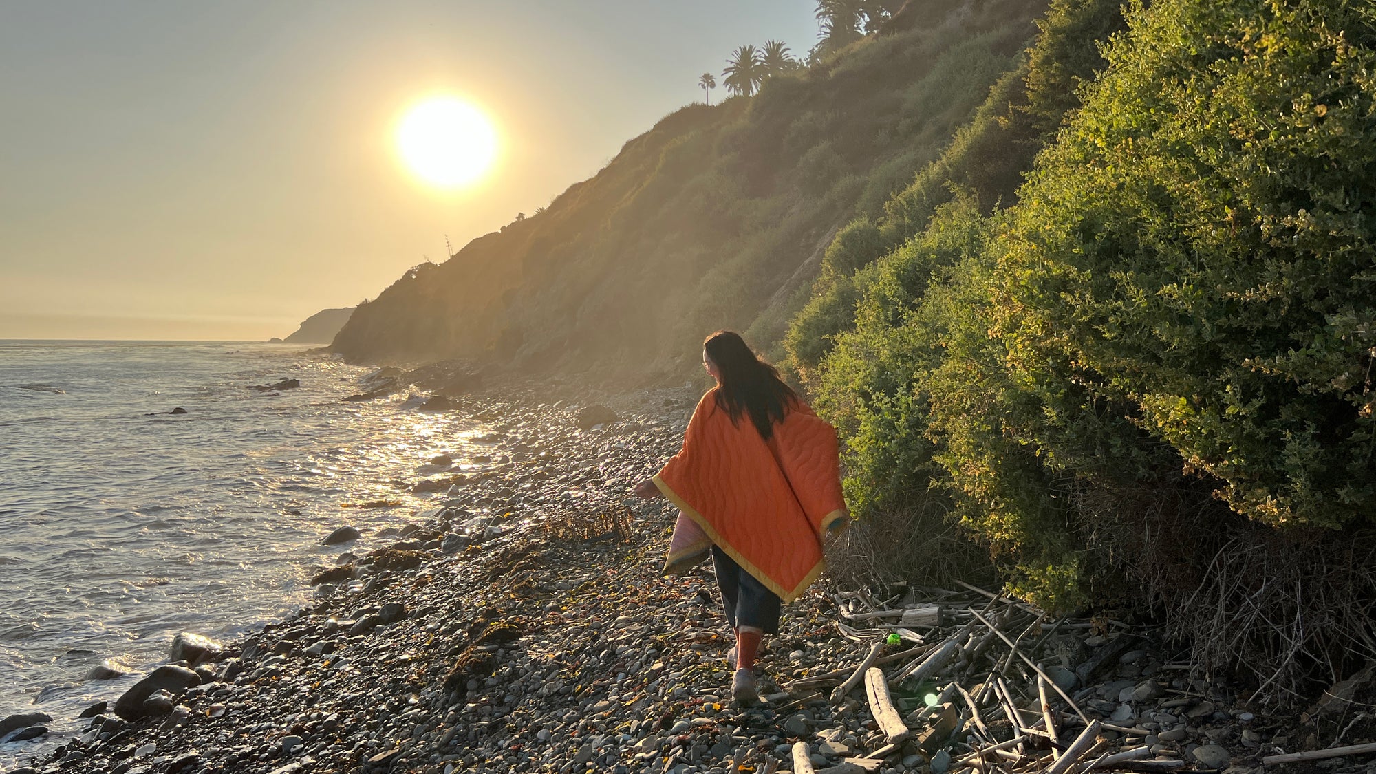 Women wearing a Scout Regalia Anywear Blanket or Poncho by the sea with the sun setting. 