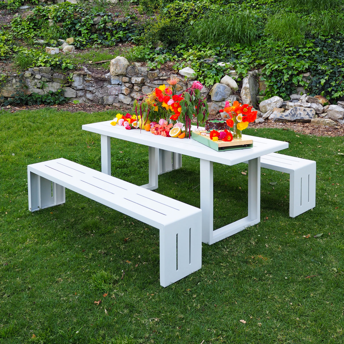 A white S.R. All Aluminum Table Set on grass with stone wall in background.