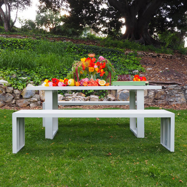 A white S.R. All Aluminum Table Set with flowers on the table, on grass with stone wall in background.