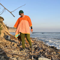 Man wearing an orange and pink poncho on the beach standing on driftwood