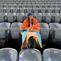 A woman sitting in an empty stadium wearing a pink and orange blanket