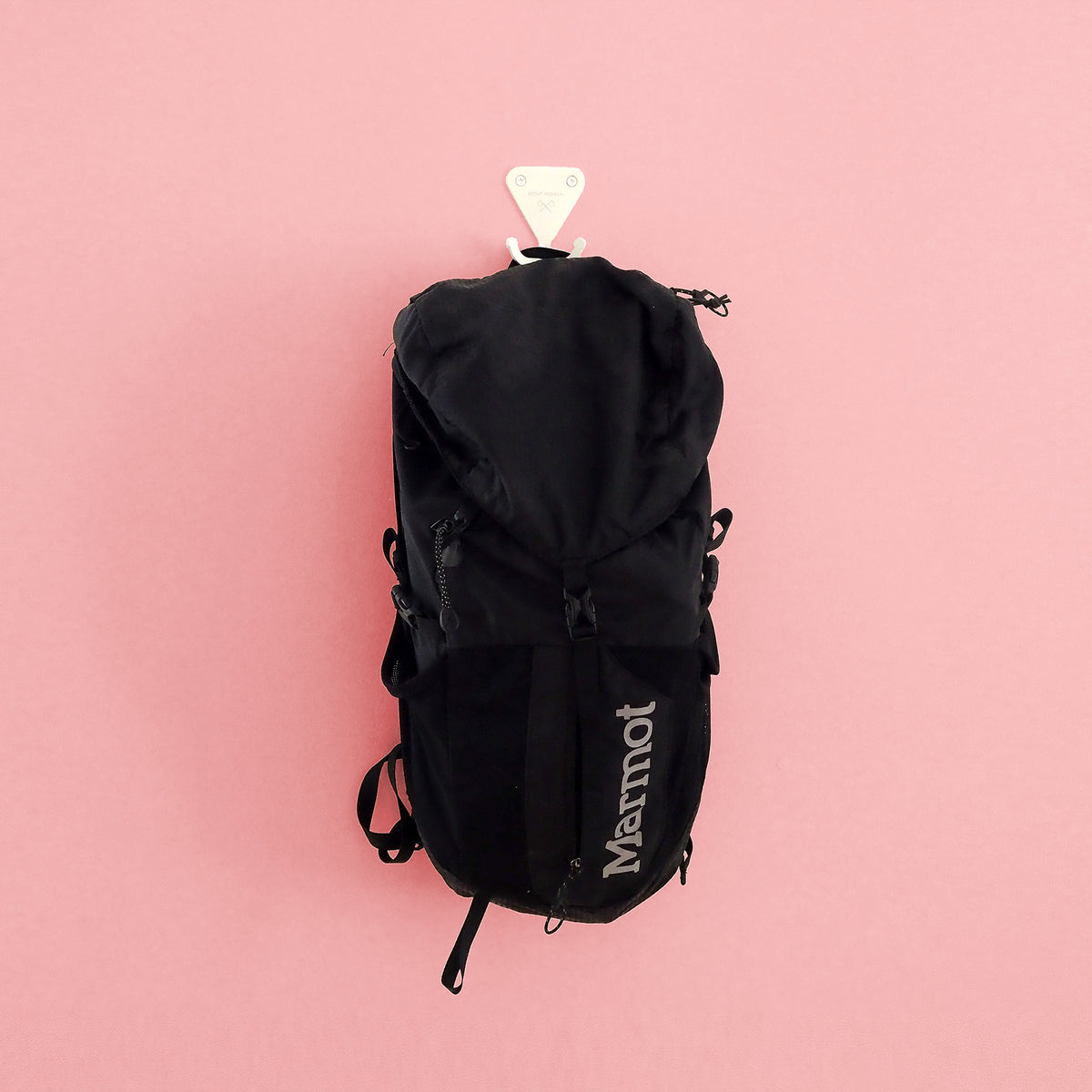 Matte white S.R. Wall Hook holding a black backpack on a pink background.