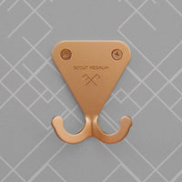 Anodized brass S.R. Wall Hook on a light grey background with geometric print.