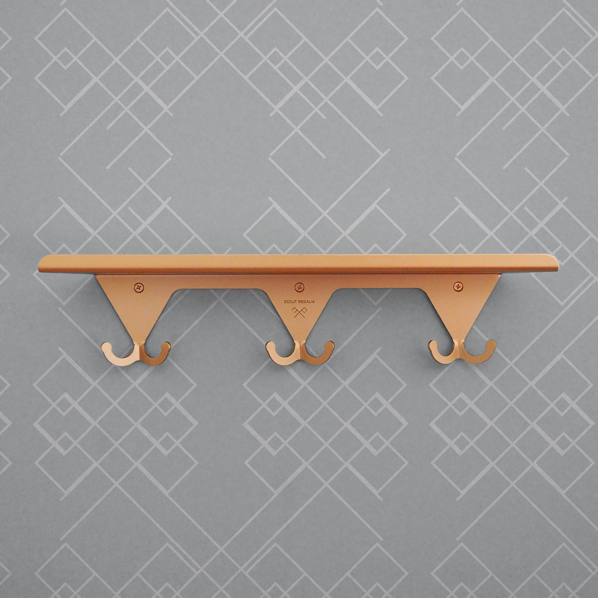 Anodized brass S.R. Wall Rack on a grey background with geometric print.