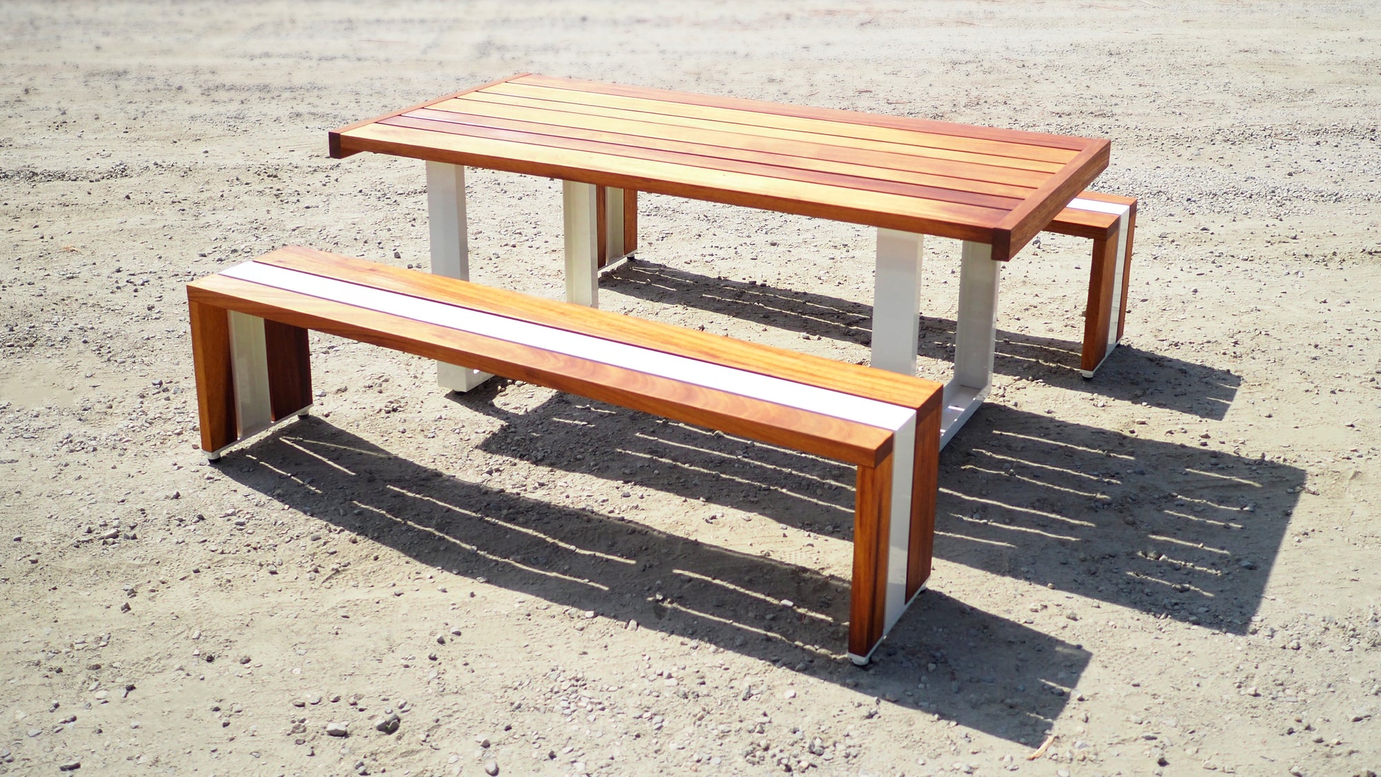 Scout Regalia Tabe Set with cream powder coated aluminum frame and  Iroko wood set on a gravel landscape.