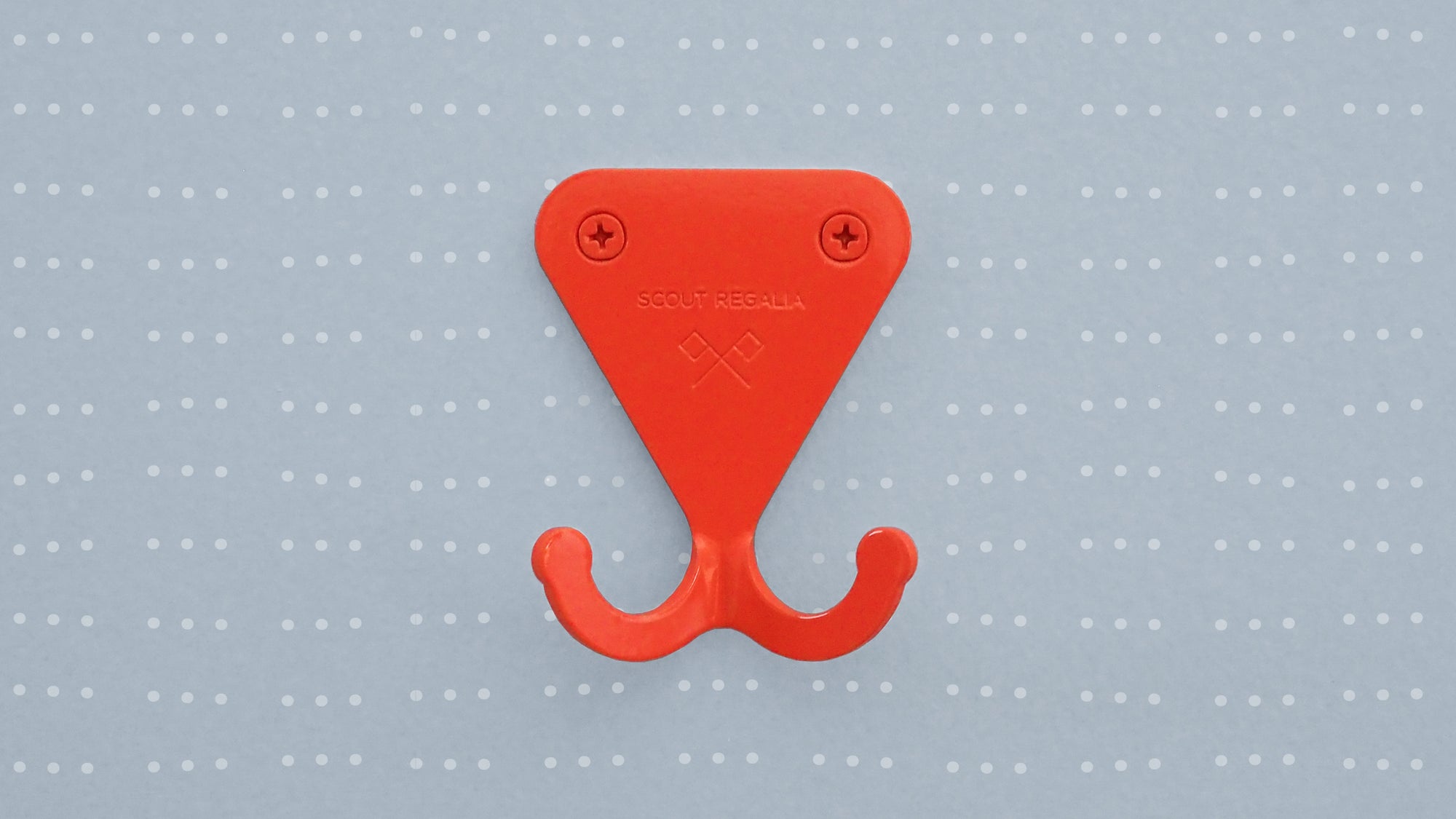 Scout Regalia Wall Hook in bright orange mounted on a light blue wallpaper with wavy dots.